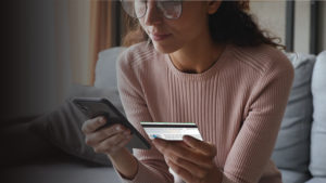woman using a smartphone and holding a debit card